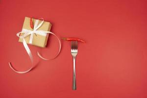 un pimiento rojo picante en un tenedor y una caja de regalo al lado foto