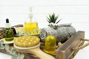 A CBD green oil, face roller, a brush for dry massage stand on a wooden tray in a bathroom photo