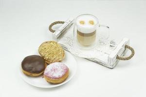 A cup of latte stands on a wooden tray for early breakfast and sweet glazed donuts photo