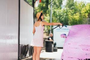 Brunette from a high-pressure hose applies a cleaner on the car photo