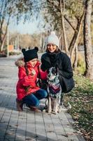 madre feliz y su hija jugando con perro en el parque de otoño foto