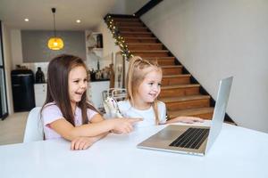 Two little girls playing together at the laptop while sitting at table photo