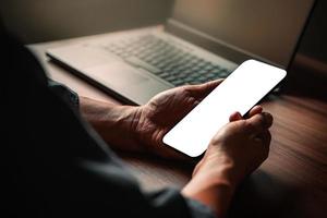 Mockup image of a man holding and using smartphone with blank desktop screen while working and drinking coffee in cafe. photo