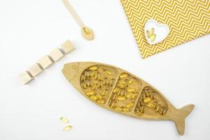 Yellow capsules of Omega 3 lie on a wooden plate in the form of the fish photo