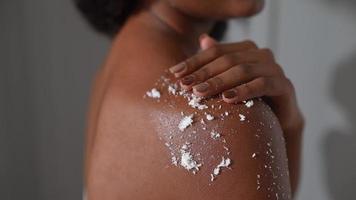 African american woman rubs scrub on shoulder skin in bathroom photo