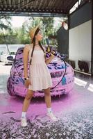 Young woman hose stands in front of a car covered in pink foam photo