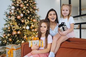 madre y dos hijas pequeñas contra el fondo del árbol de navidad foto