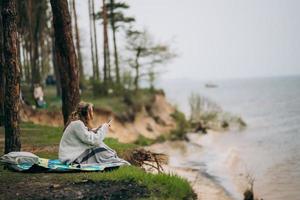 A young woman sits on the shore of a small lake near the forest. photo