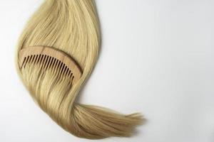 A strand of blonde hair with a wooden comb on it lying on a white background photo