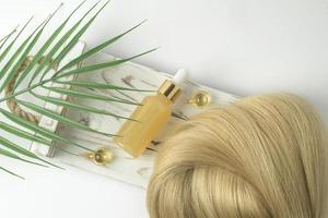 Natural blonde hair strand and essential oil for hair treatment in golden capsules lying on a white wooden tray photo