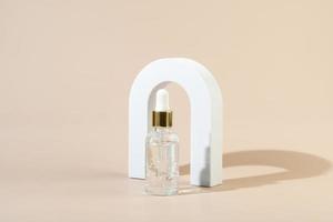 A transparent natural organic serum or essential oil for face care standing in a white arch on a beige background photo