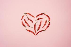 Red hot chilli peppers in the form of the heart lie on a pink background table photo