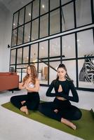 Two young women meditating in lotus pose with hands in namaste. photo