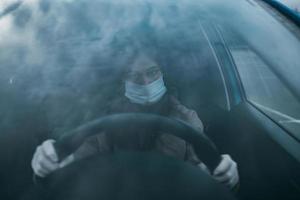 mujer joven con una máscara y guantes conduciendo un automóvil. foto