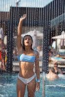 hermosa chica en traje de baño duchándose bajo el agua en la playa del resort. foto