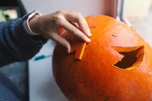 Hand of a young woman cutting out a Halloween pumpkin photo