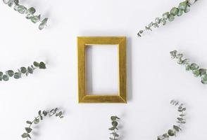 A golden frame for copy space and green leaves of eucalyptus around on a white background. Copy space photo