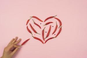 pimientos picantes rojos en forma de corazón yacen sobre una mesa de fondo rosa foto