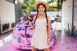 Young woman hose stands in front of a car covered in pink foam photo