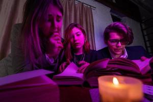 Two women and a guy are reading a mysterious books, close view photo