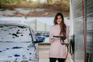 Brunette from a high-pressure hose applies a cleaner on the car photo