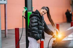 Young beautiful woman traveling by electric car having stop at charging station photo