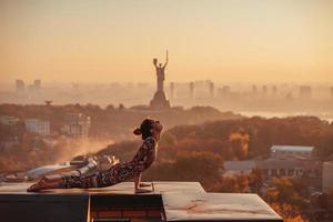 Woman doing yoga on the roof of a skyscraper in big city. photo