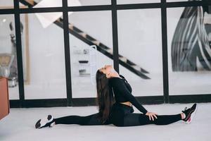 Young female wearing black sports suit exercising yoga pose indoors. photo