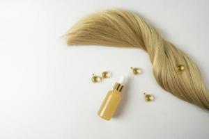 A natural essential oil or serum for hair care in golden capsules lying on a white table. Hair care and smoothing concept photo