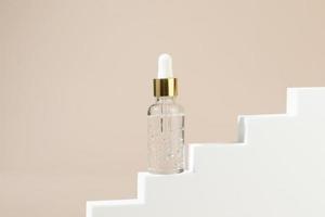 A dropper bottle with the transparent natural gel or oil, serum for face standing on a white stairs photo