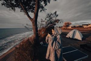 mujer joven toma fotos de la puesta de sol del mar por teléfono inteligente