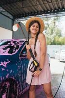 Woman with hose stands by car covered in pink foam photo