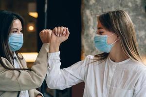 Co-workers in protective masks giving high five with elbows. photo