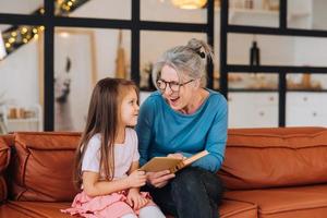 Nice elderly woman grandmother reading story to granddaughter. photo