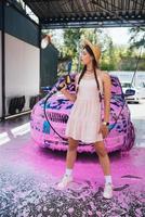 Young woman hose stands in front of a car covered in pink foam photo