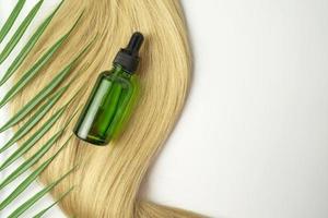 A  dropper bottle of green CBD oil or serum for hair care in golden capsules lying on a strand of  blonde hair. Hair care and smoothing concept photo
