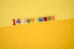 November 14 on a yellow, paper background with multicolored and wooden letters and space for text. photo