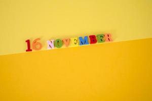 16 de noviembre sobre un fondo de papel amarillo con letras multicolores y de madera y espacio para texto. foto