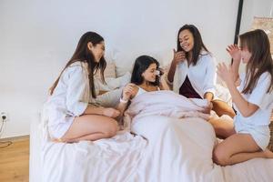 Positive young girls women friends indoors on bed at the hen party at home. photo