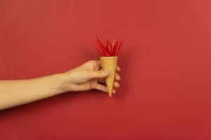 A womans hand holds mini red hot peppers in the waffle cone on a red background photo