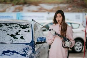 Brunette from a high-pressure hose applies a cleaner on the car photo