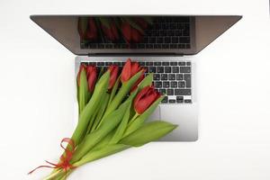 los tulipanes rojos yacen en una computadora portátil para el día internacional de la mujer foto