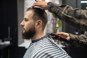 Master in barbershop makes men's haircutting with hair clipper photo