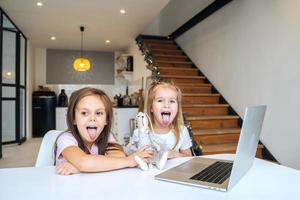 Two little girls playing together at the laptop while sitting at table photo