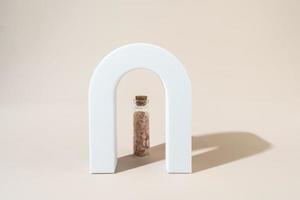 Two glass bottles with pink sea salt for spa procedures for face or body standing between geometric forms photo