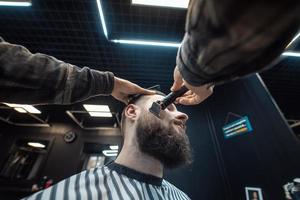 Barber works with a beard clipper. Hipster client getting haircut. photo