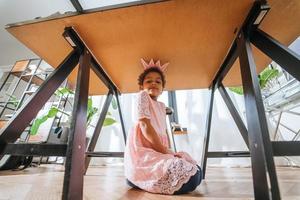 Little girl is playing under the table tongue in the camera photo