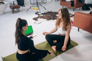 Two young women meditating in lotus pose at home photo