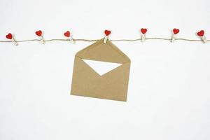 un sobre marrón con una carta en blanco cuelga de la cuerda con alfileres de corazón rojo foto