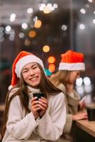 Girl wearing Santa hat sitting in coffee shop and drinking coffee photo